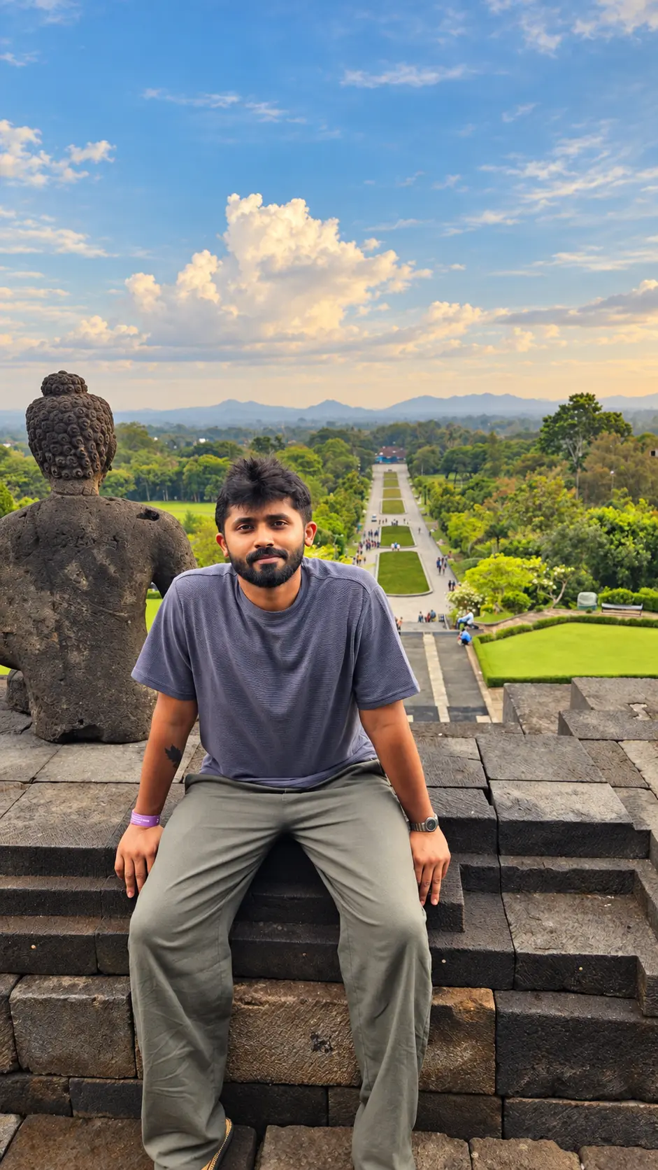 Terry seated before a Buddha statue on landscaped temple grounds